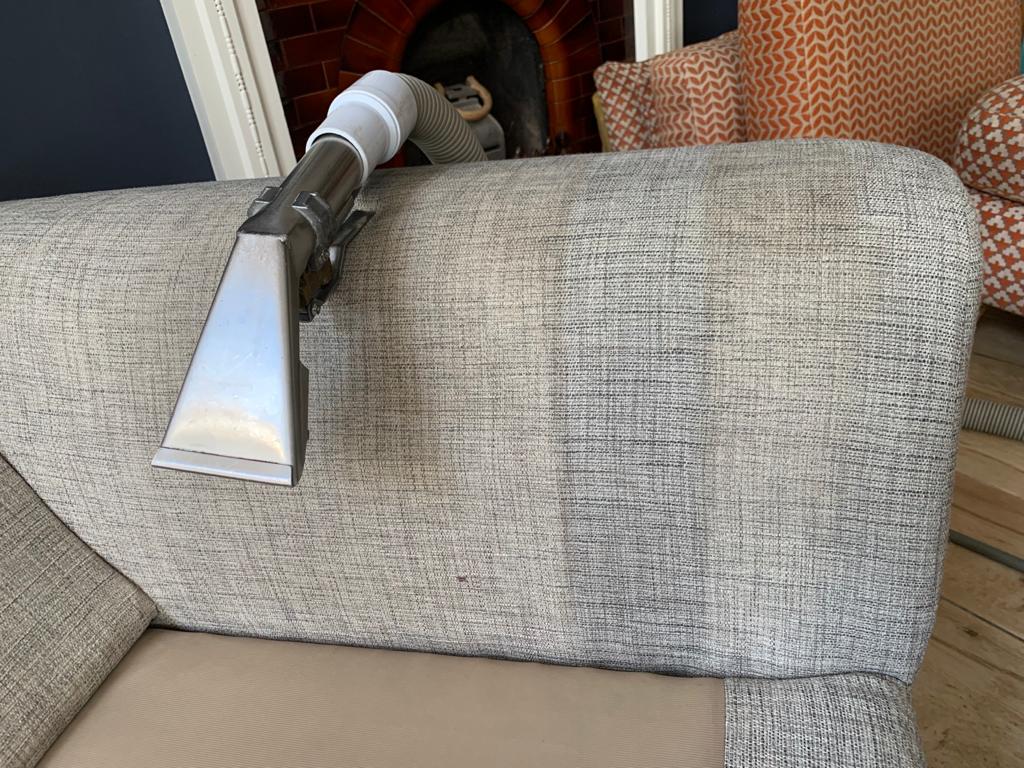 This is a photo of an arm of beige sofa that shows a test patch that has been steam cleaned. The steam cleaning machine is also showing in the photo works carried out by Tooting Carpet Cleaning