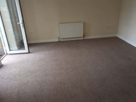 This is a photo of a living room after it has been cleaned. The room is empty and has a brown carpet that has been steam cleaned works carried out by Tooting Carpet Cleaning